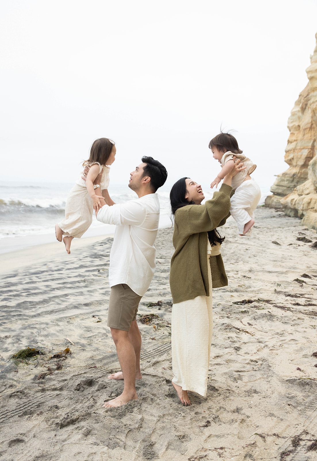 Two parents lifting their small children into the air on a San Diego beach during a family session