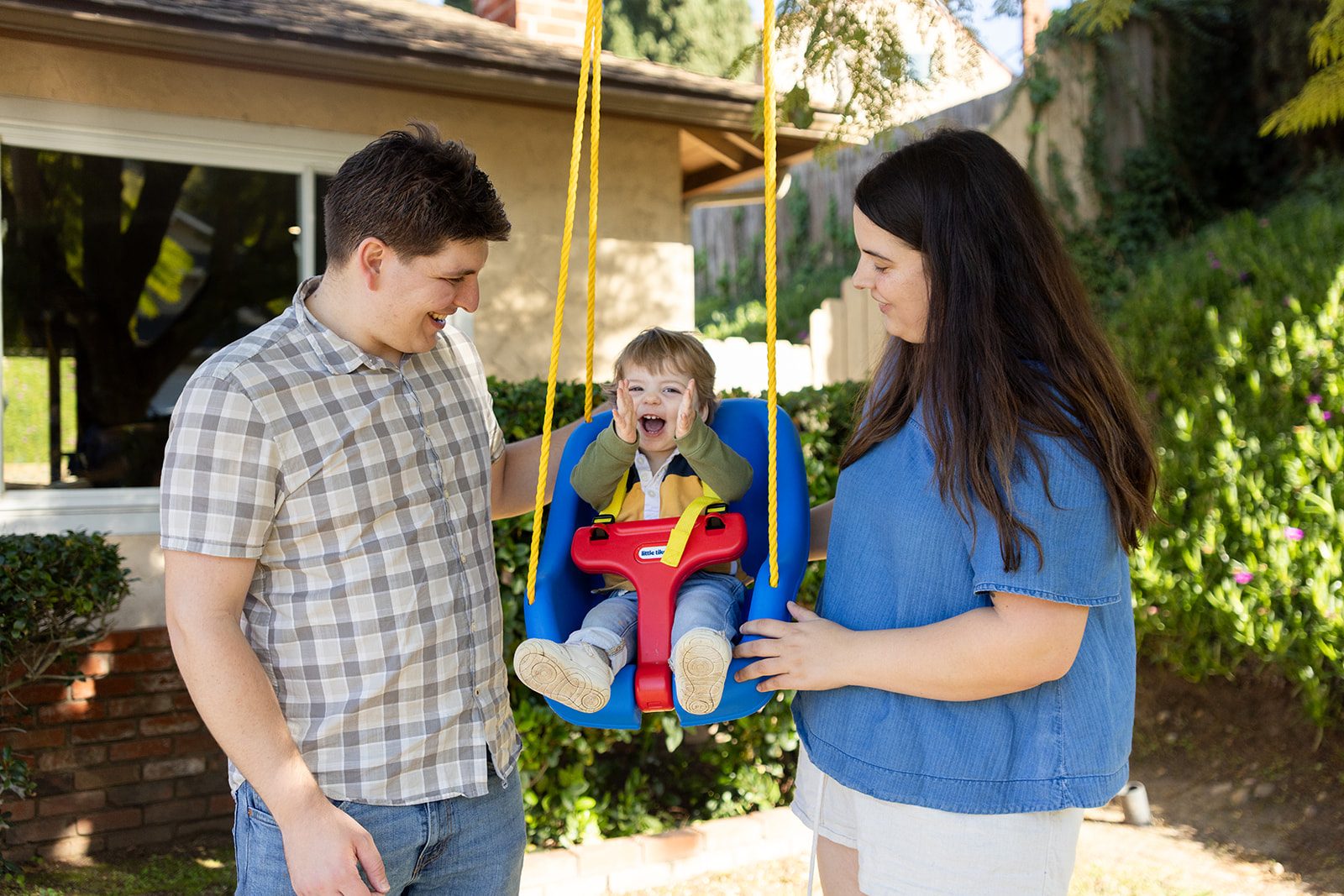 Parents pushing their laughing toddler on a garden swing during a San Diego family session