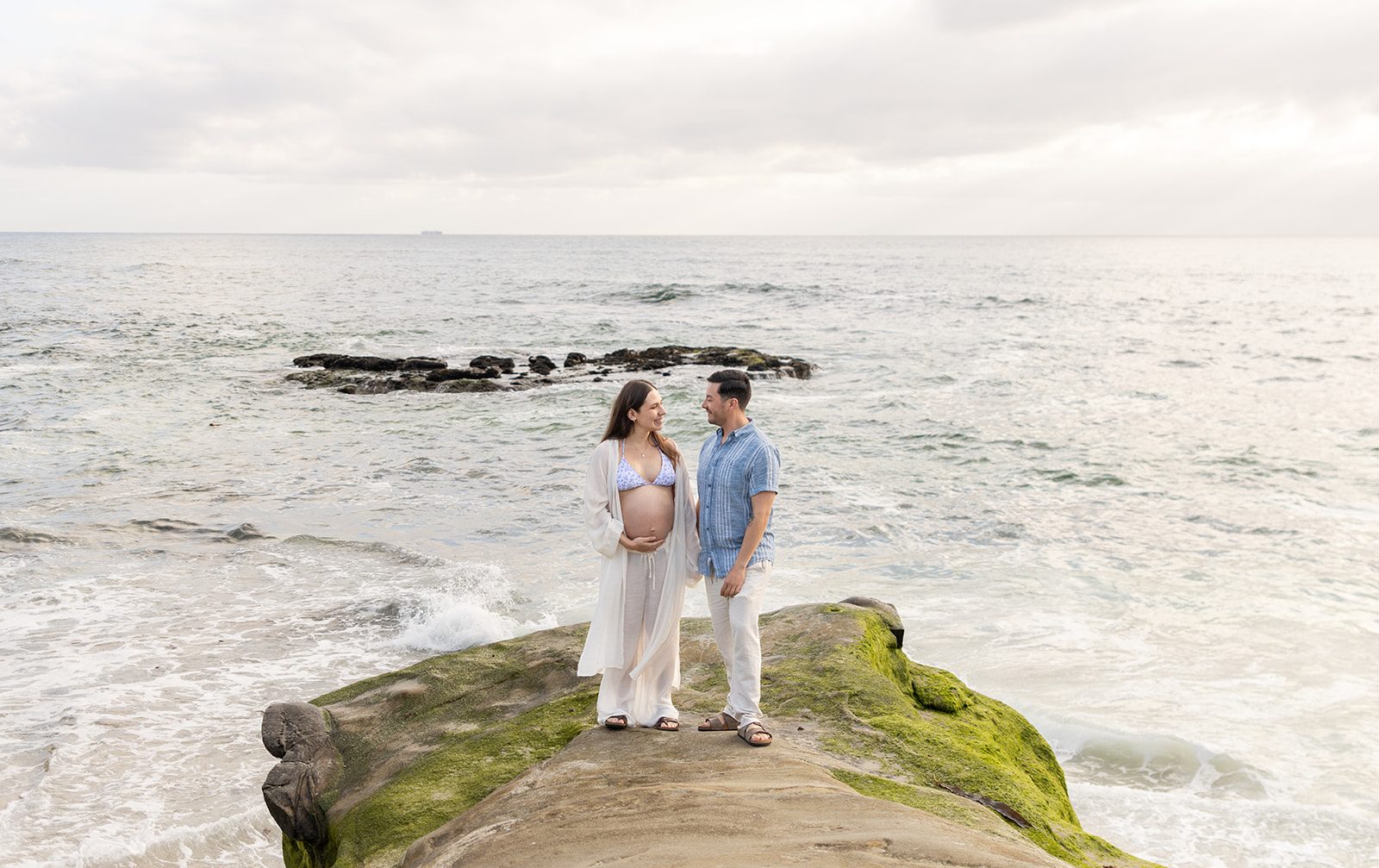 Couple standing on the rocks above the water during a San Diego maternity photoshoot