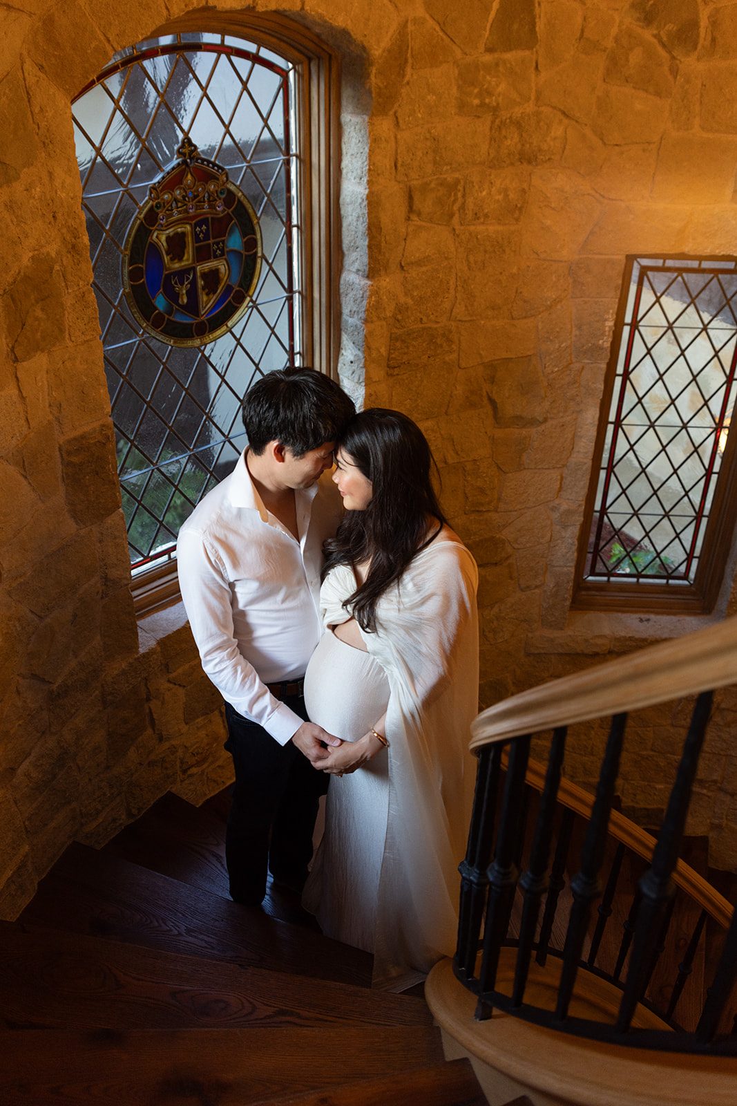 Expecting couple embrace by a stained glass window during an at-home San Diego maternity session