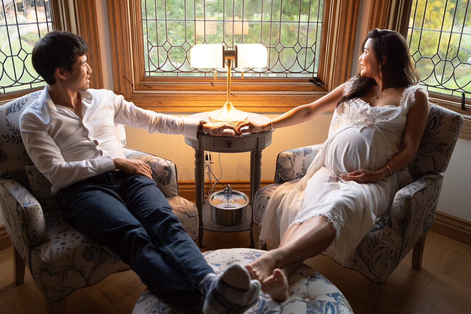 Couple sitting together at home in warm lamplight during a maternity photoshoot