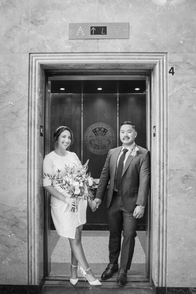 Groom giving cheek kiss to bride on elopement day at San Diego courthouse.