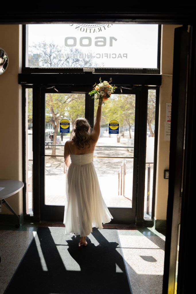 Bride throwing flowers into air walking out of San Diego courthouse to go elope.