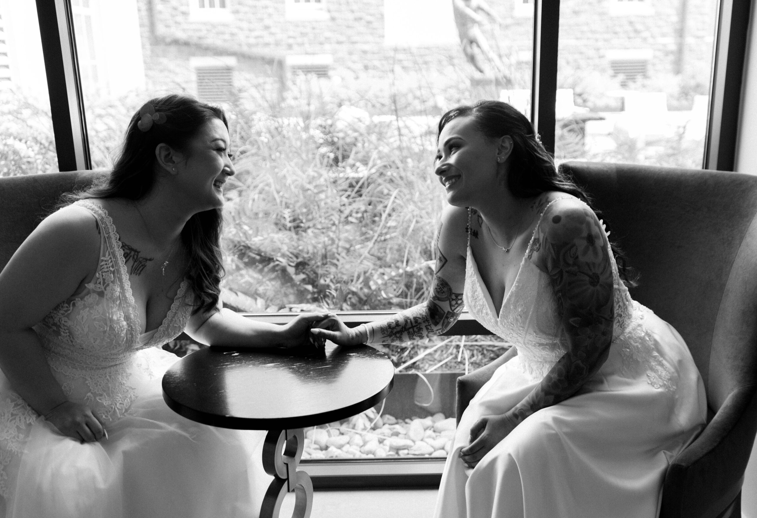 Two brides hold hands and look at each other on wedding day