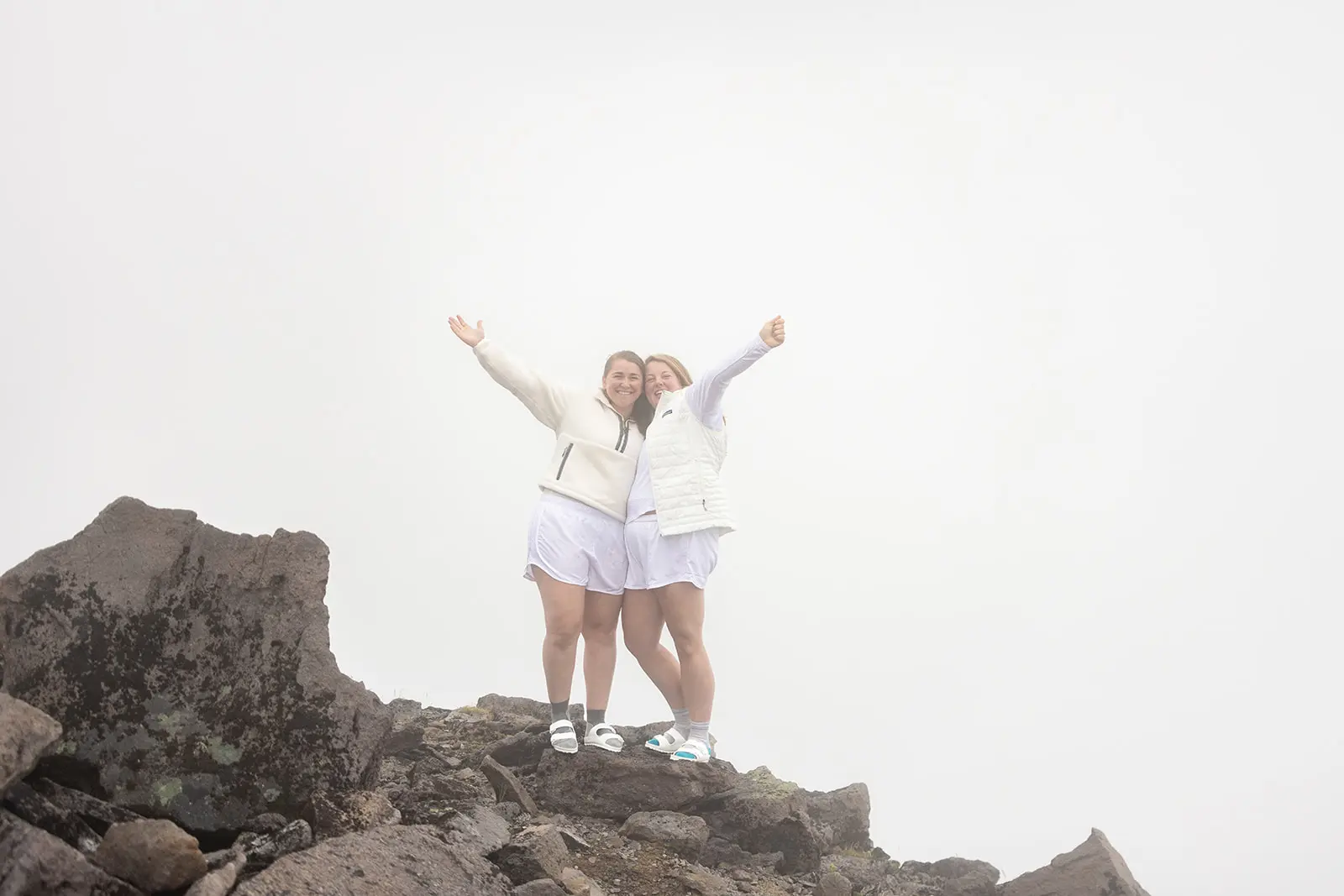 Couple raising their arms in celebration on the foggy volcanic summit of Burroughs Mountain Trail, Mt. Rainier