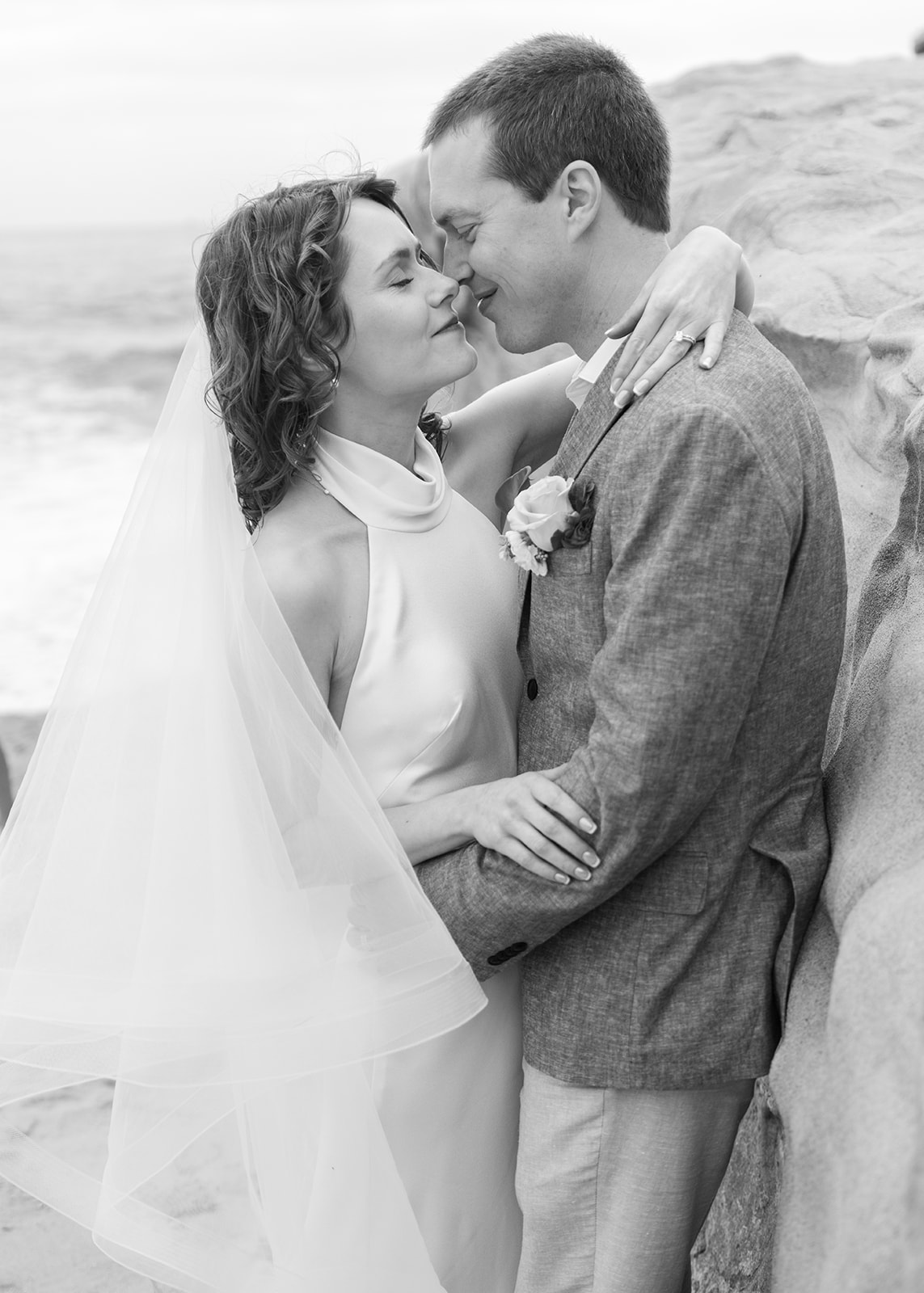 Newly married couple kissing on the beach, veil catching the light, after their courthouse ceremony