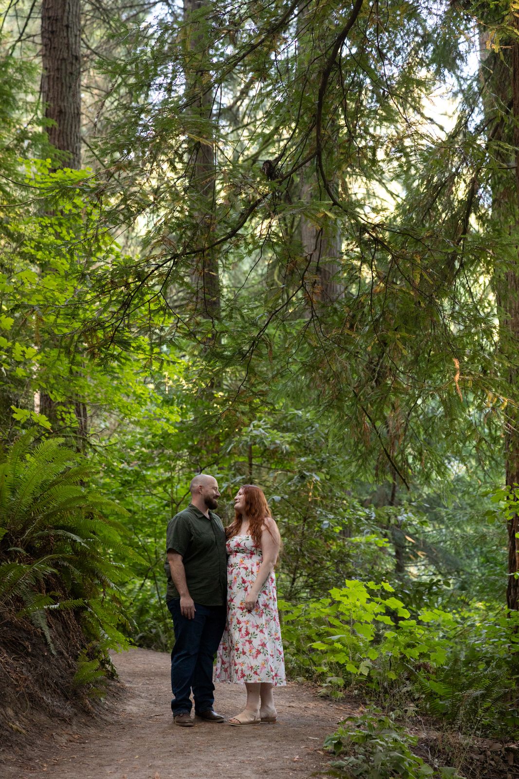Couple standing together on a forest trail beneath tall firs at Hoyt Arboretum in Portland