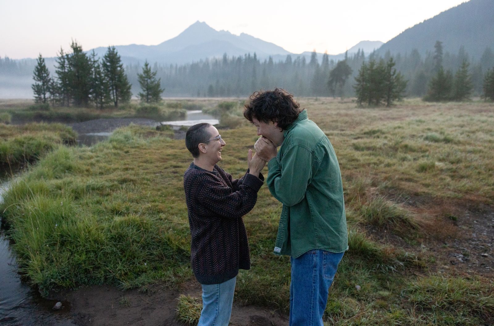 Couple laughing together in a Central Oregon meadow at sunrise during their engagement session