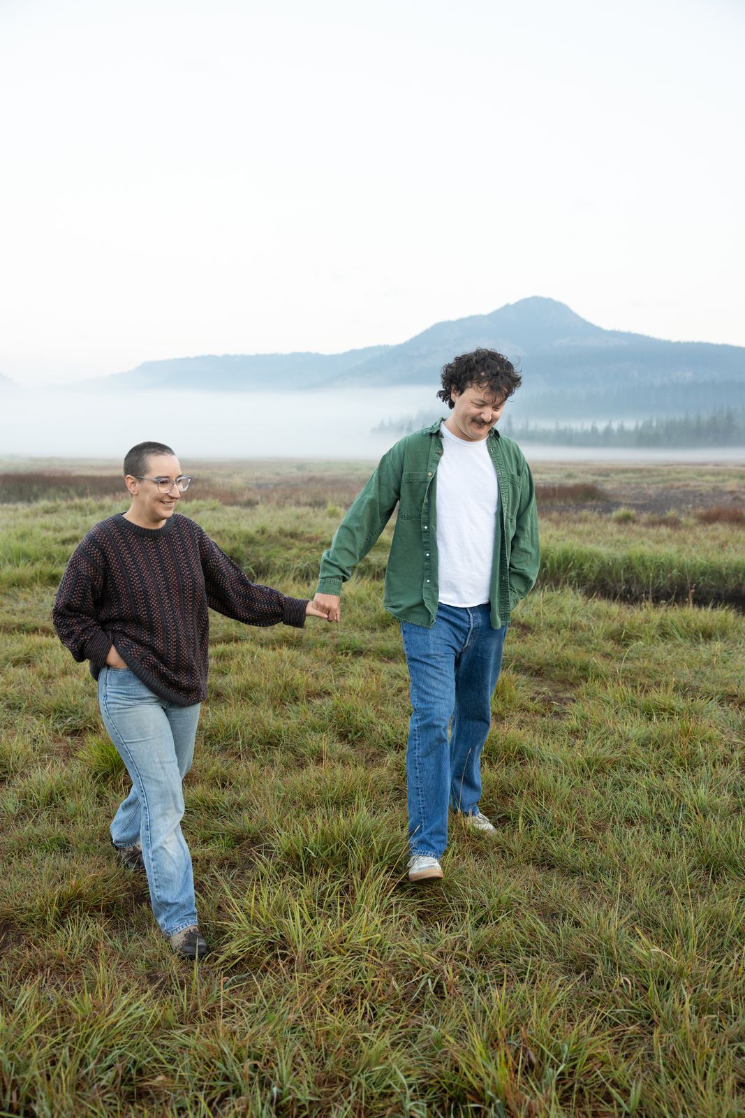 Engaged couple walk hand in hand through a foggy meadow at sunrise near Sparks Lake Oregon