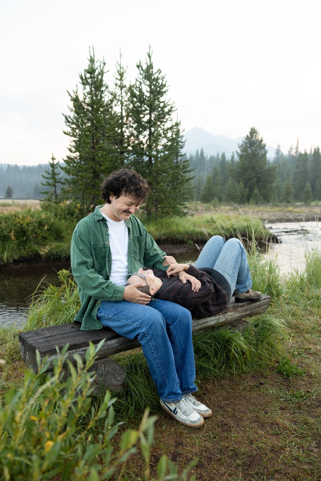Couple sit together on a log bench in a meadow at sunrise near Sparks Lake