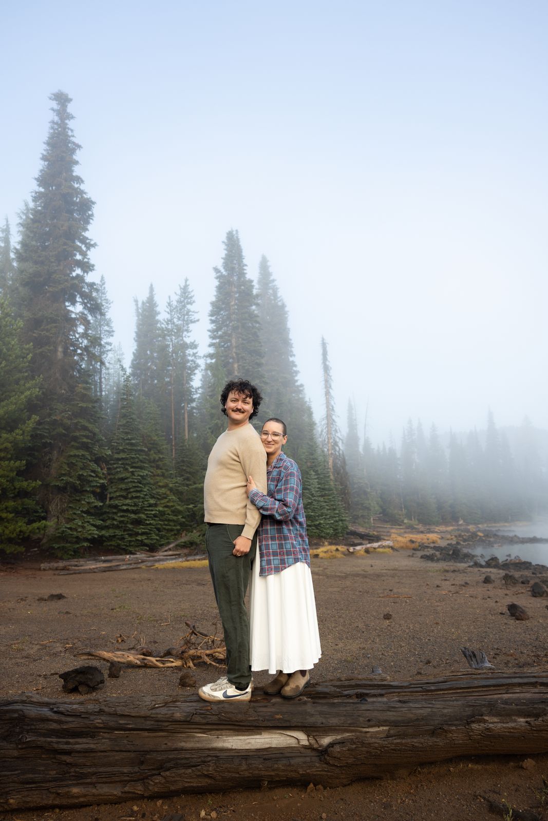 Engaged couple stand together on the fogged shoreline of Sparks Lake in Central Oregon