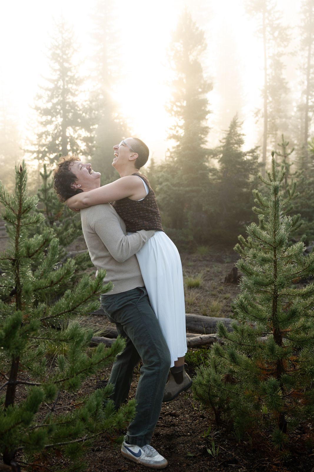 Couple embrace in golden light as fog burns off through the trees at Sparks Lake