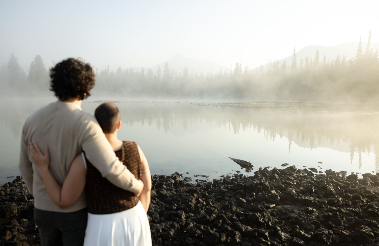 Couple hold each other on the rocky shore of Sparks Lake as the fog begins to lift
